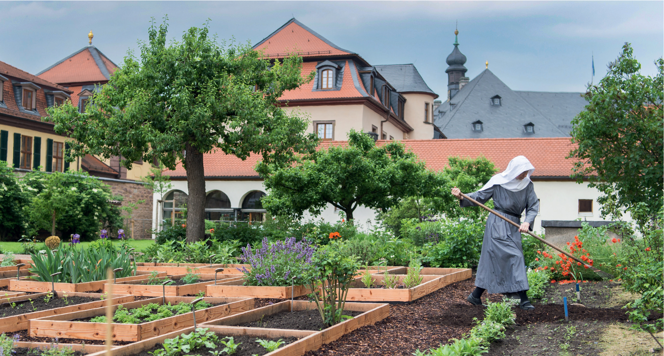 Eine Schwester bei der Arbeit im Nutzgarten mit Gemüse, Salat, Beeren- und Baumobst im Klostergarten der Abtei zur Hl. Maria.